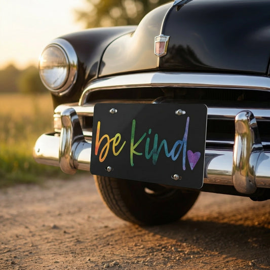 Vintage car with a 'be kind' license plate on a dirt road.
