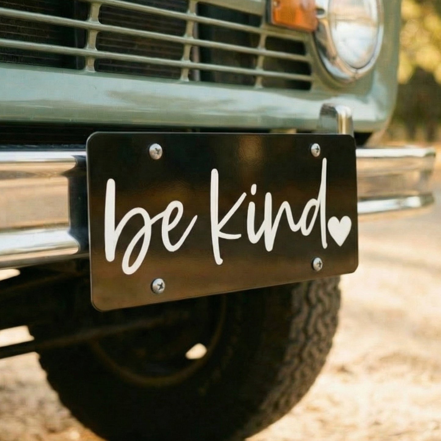 Vintage truck with 'be kind' license plate on a road.
