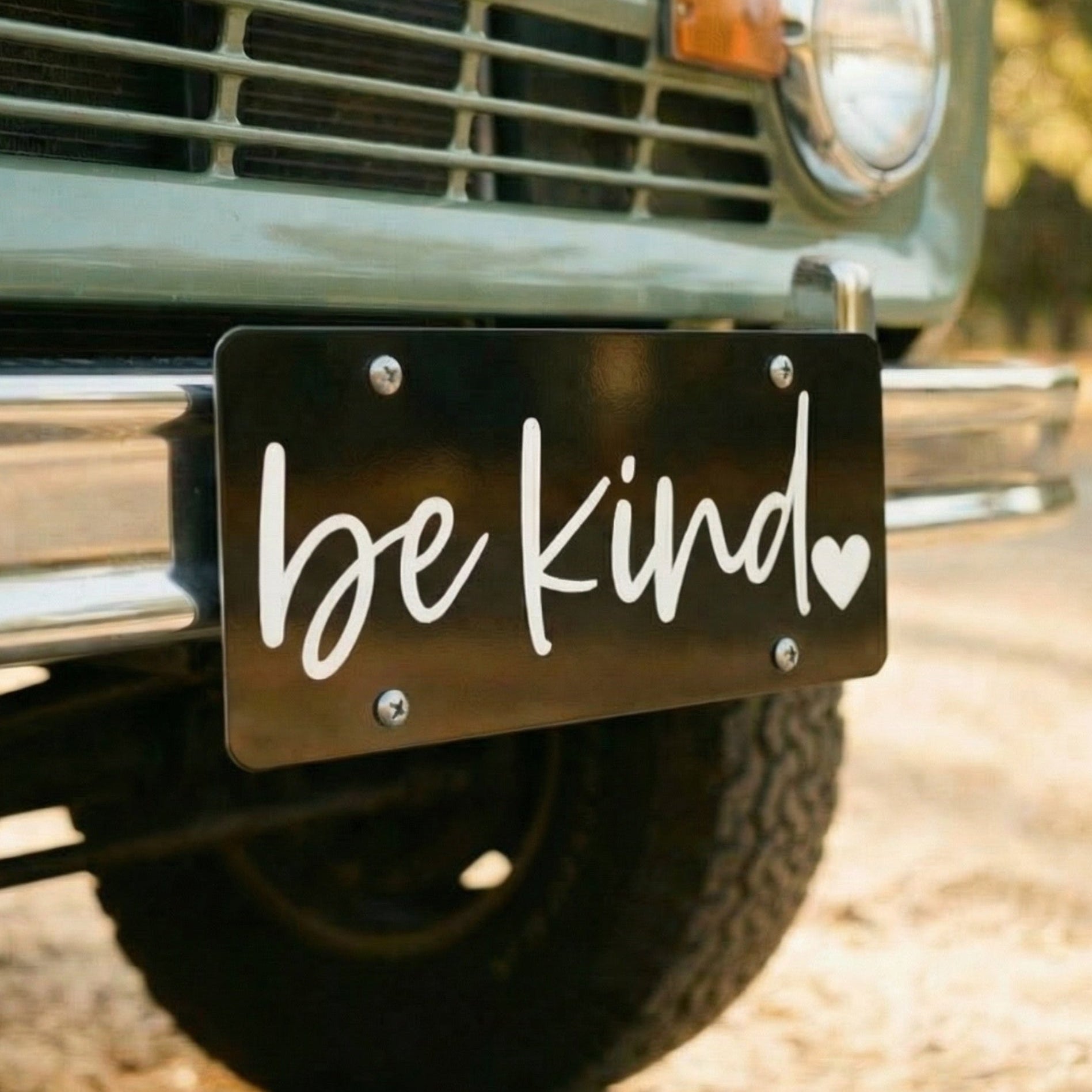 Vintage truck with 'be kind' license plate on a road.