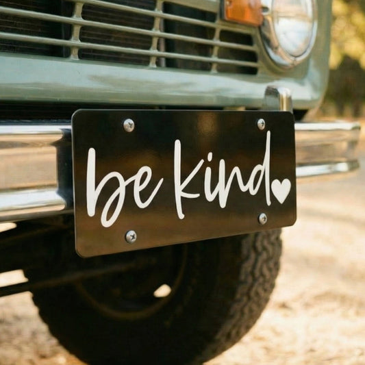 Vintage truck with 'be kind' license plate on a road.