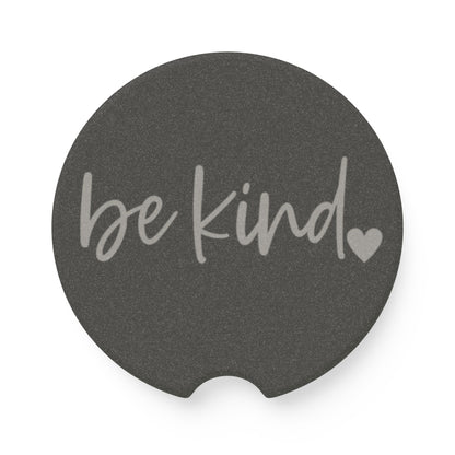Round dark gray coaster with 'be kind' text and heart symbol on a white background