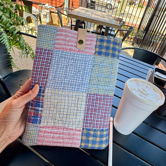 Hand holding one-of-a-kind rescued vintage quilt book and iPad sleeve with leather snap closure outdoors.