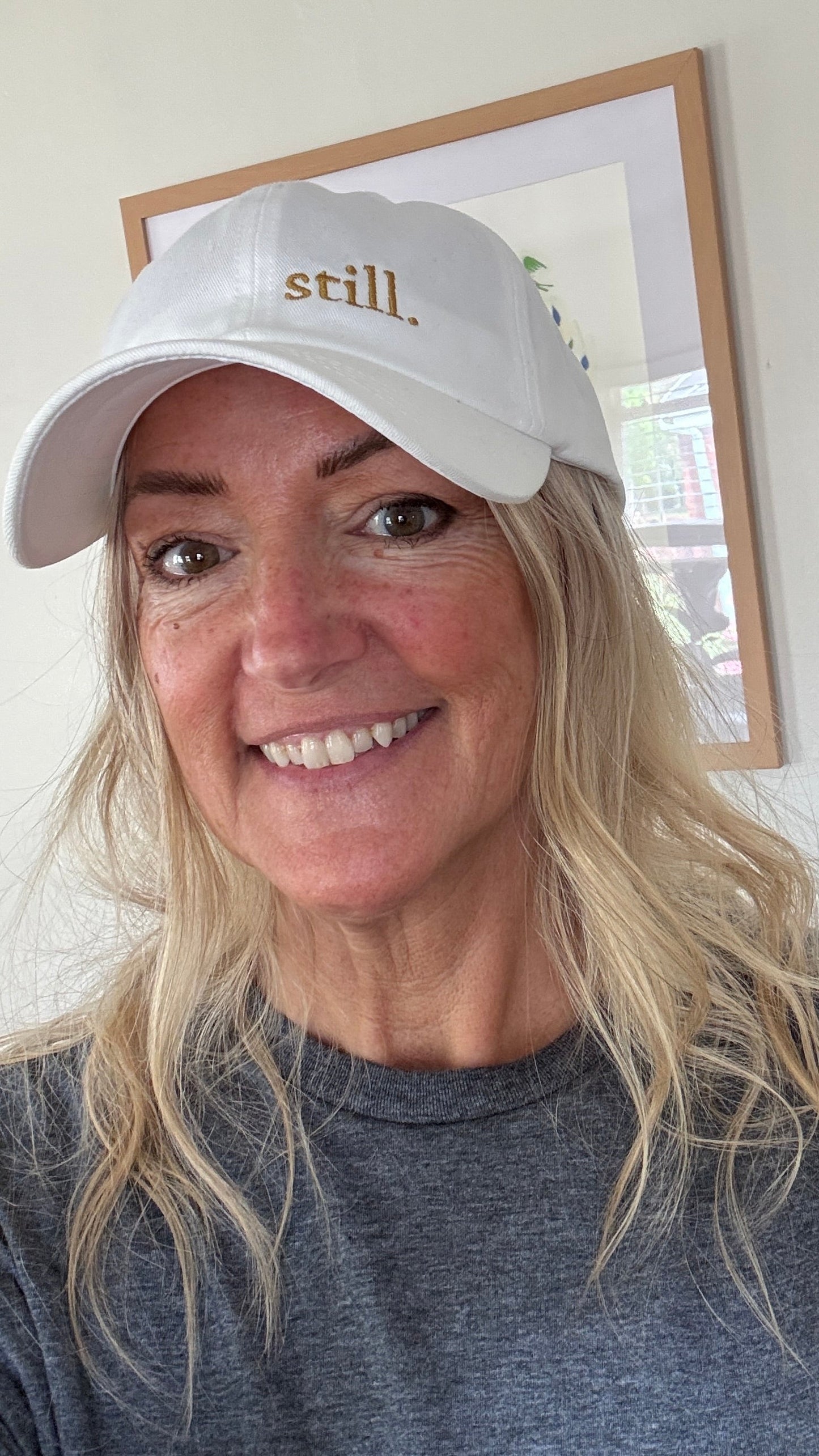 Woman wearing a white embroidered “still.” baseball hat in soft natural light, casual everyday outfit, calm and minimal style