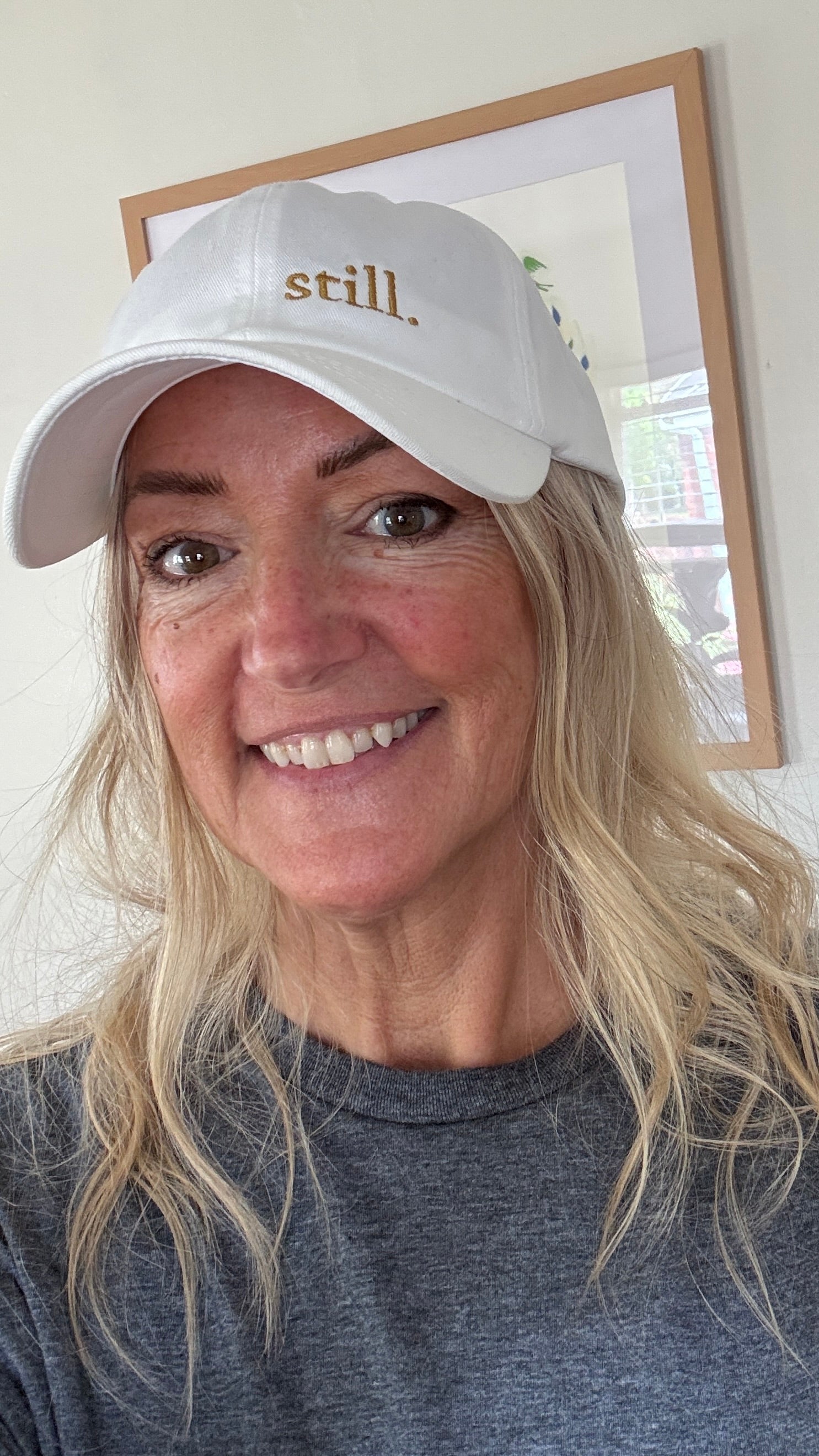 Woman wearing a white embroidered “still.” baseball hat in soft natural light, casual everyday outfit, calm and minimal style