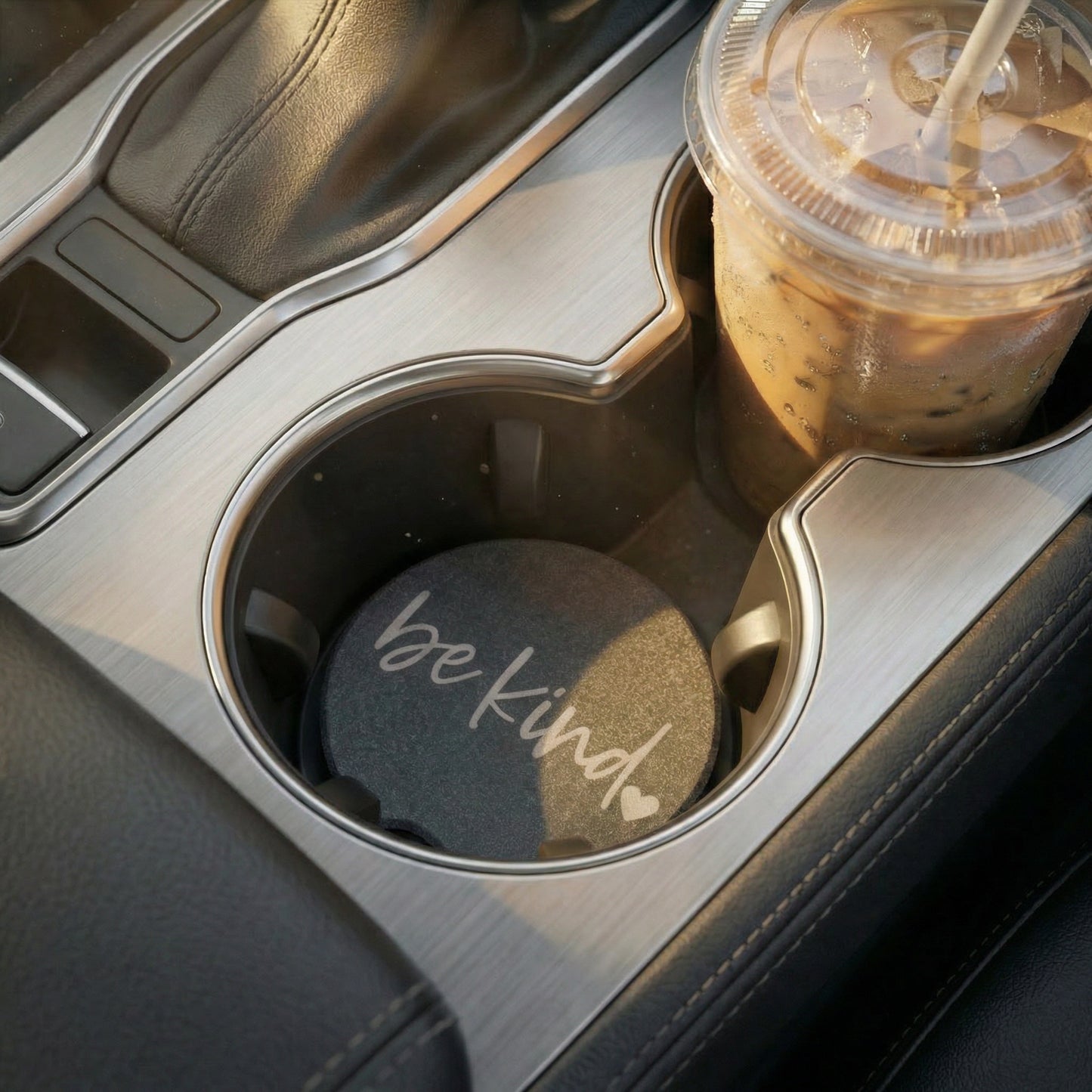 Car cup holder with a drink and a coaster with 'be kind' text