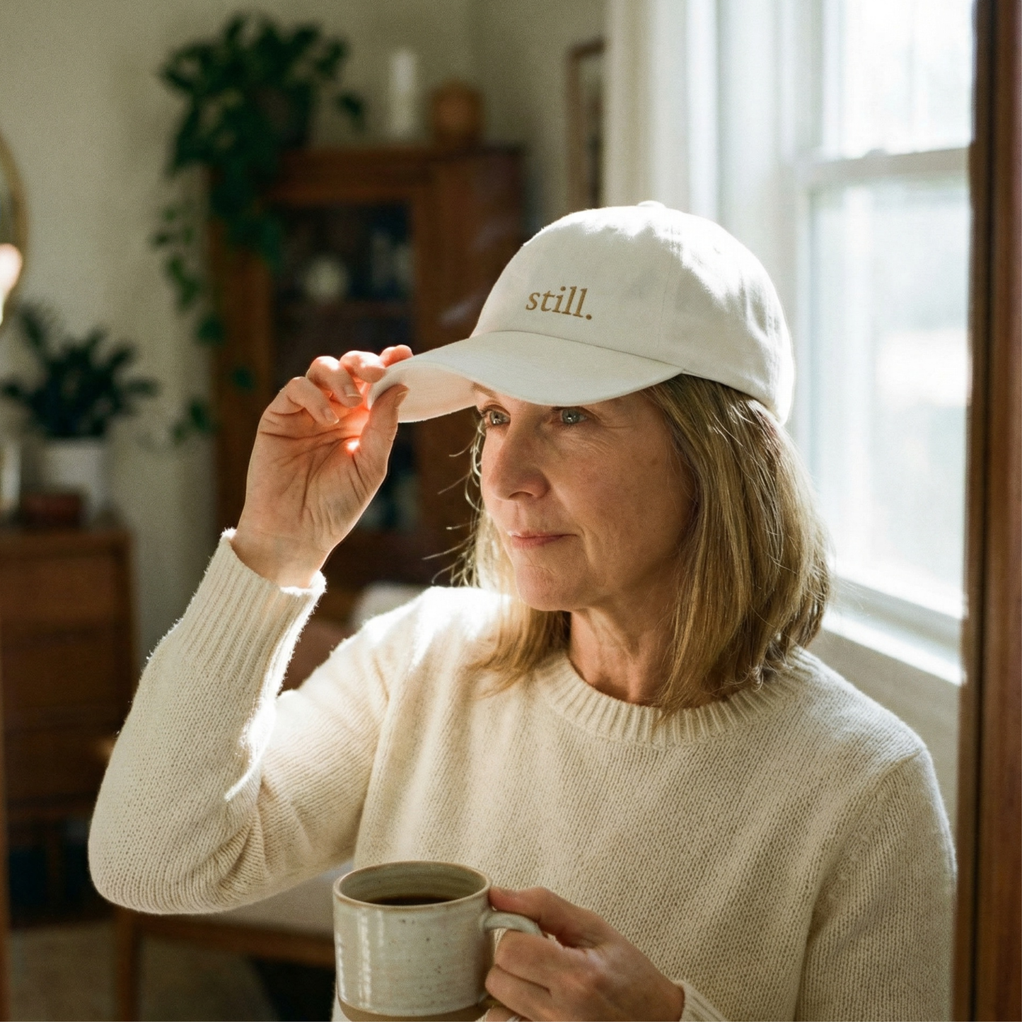 White embroidered dad hat with the word “still” worn by a woman in natural morning light.