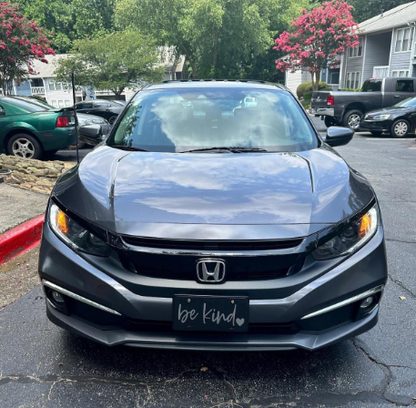 Black Be Kind plastic license plate installed on black Honda sedan