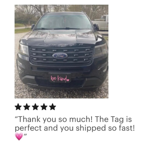 Black Be Kind plastic license plate with pink script lettering installed on black Ford SUV
