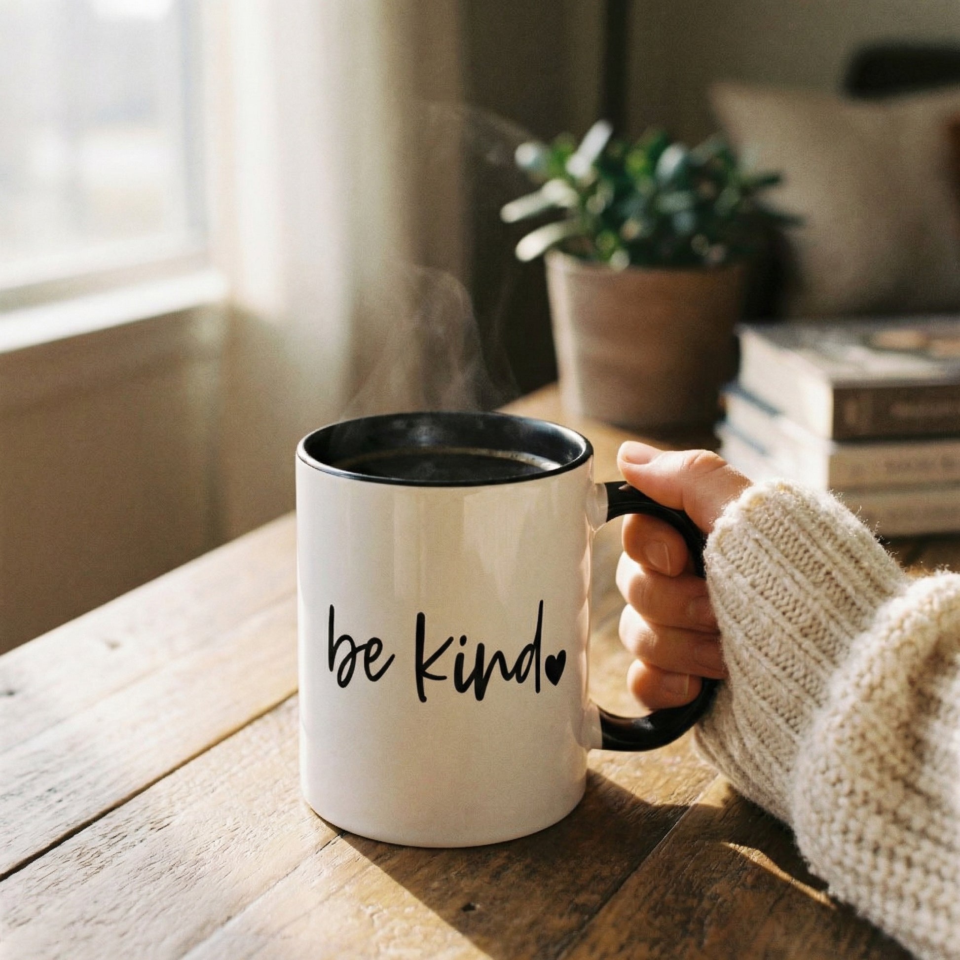 Person holding a mug with 'be kind' text in a cozy indoor setting