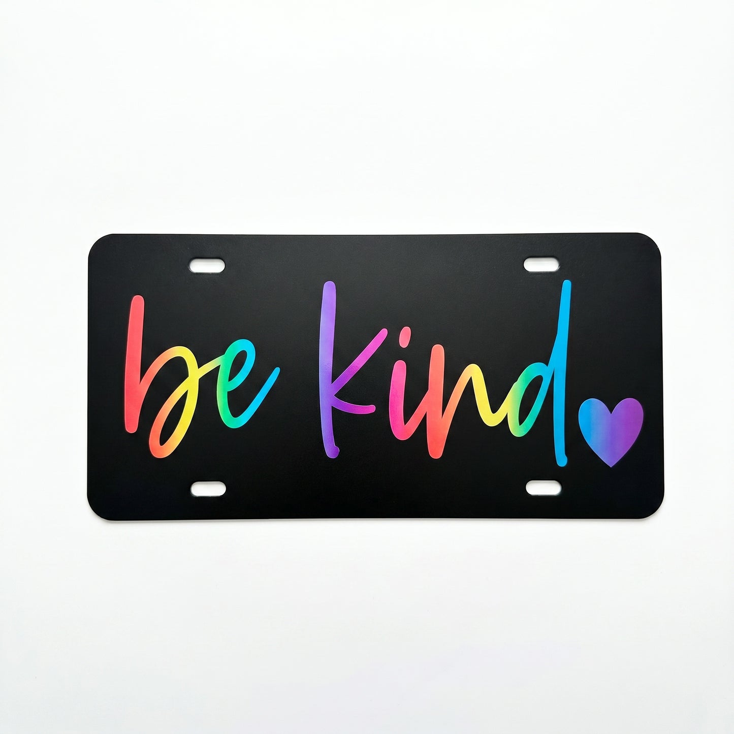 Black Be Kind plastic license plate with rainbow script lettering and matching heart detail on white background