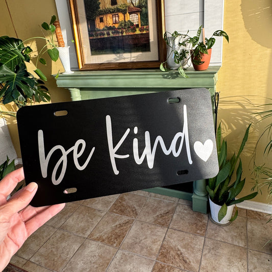 black plastic license plate with be kind in white lettering