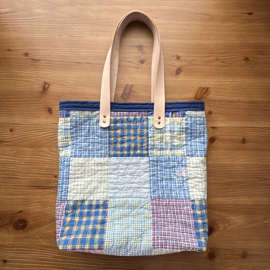 One-of-a-kind rescued vintage quilt market tote with vegetable-tanned leather handles on a wood surface.