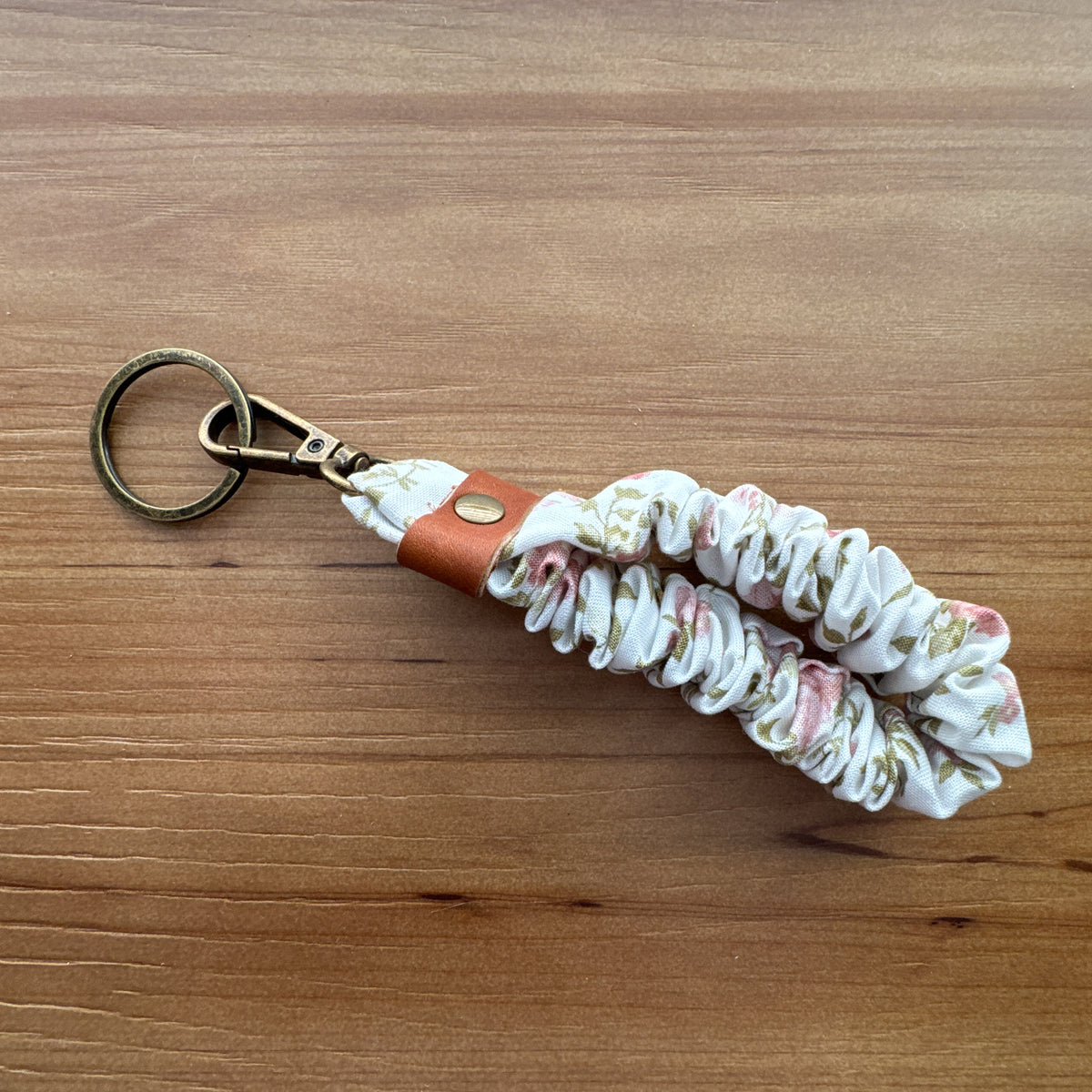 Close-up of Cottage Roses scrunchie wristlet keychain showing gathered fabric, leather accent, and antique brass-tone hardware.