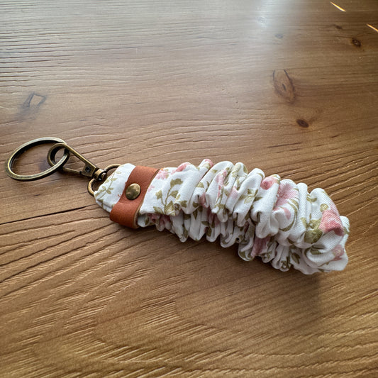 Handmade scrunchie wristlet keychain in cream floral fabric with leather accent and antique brass-tone hardware.