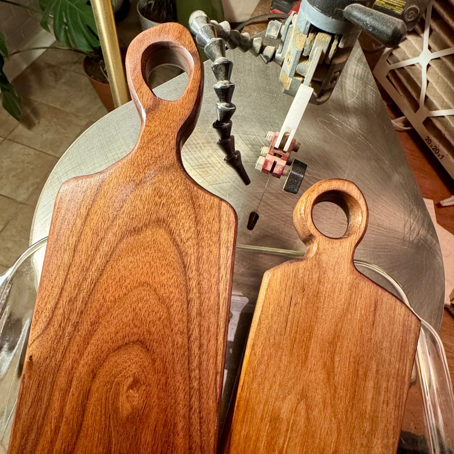 Handmade walnut serving boards in the workshop, showing two sizes beside the scroll saw used to shape them.