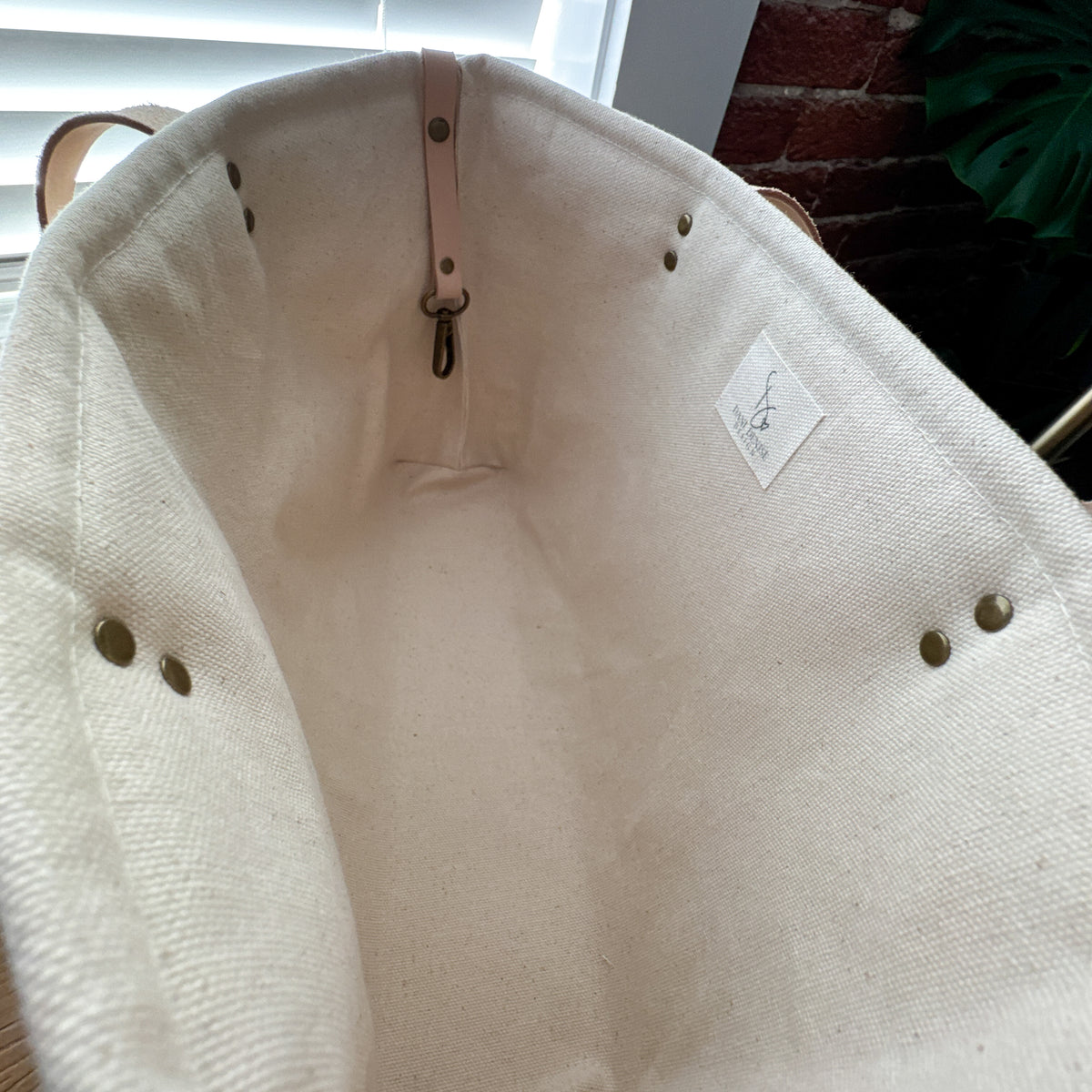 Interior of botanical market tote showing cotton lining, vegetable-tanned leather key keeper, metal hardware, and Dani Denise Design label.
