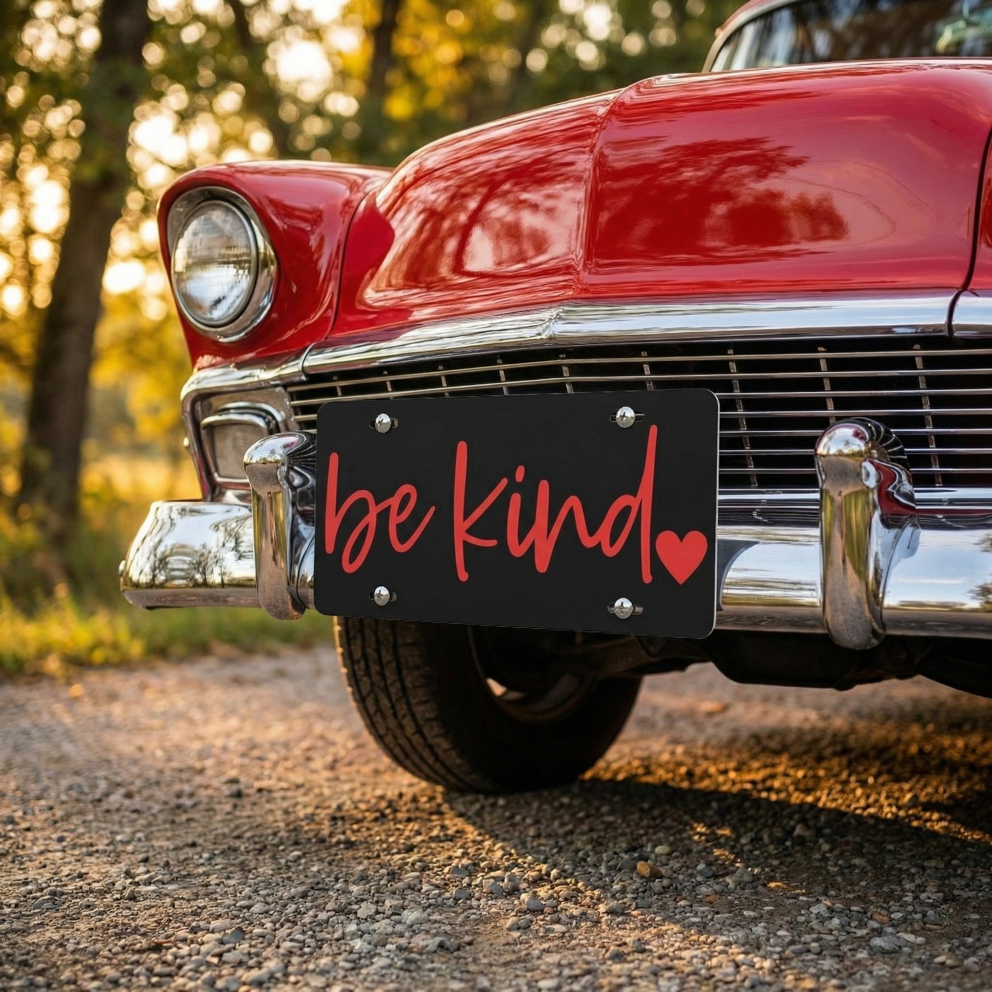 Vintage red car with 'be kind' license plate in a natural setting