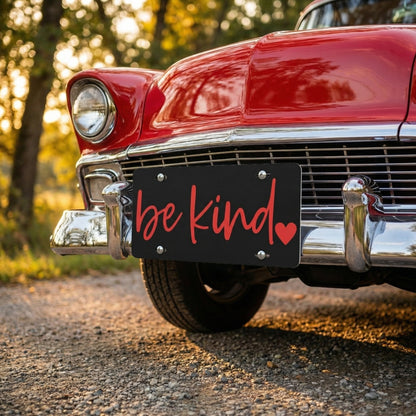 Vintage red car with 'be kind' license plate in a natural setting
