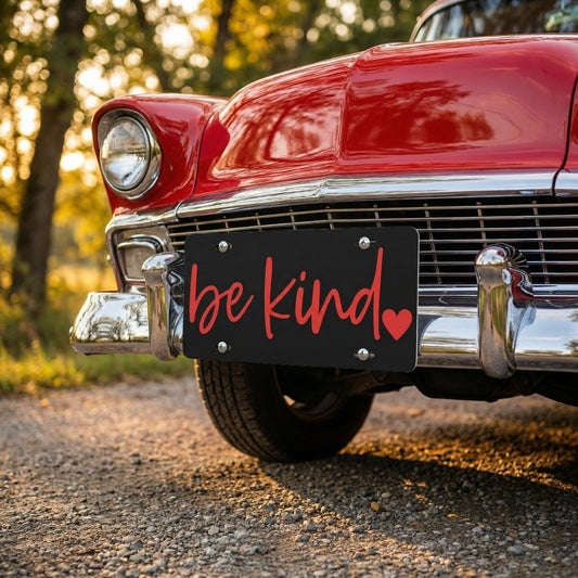 Vintage red car with 'be kind' license plate in a natural setting