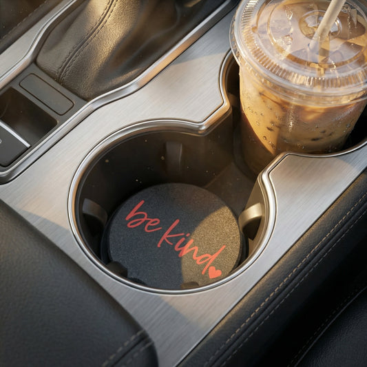 Car cup holder with a drink and a coaster with 'be kind' text