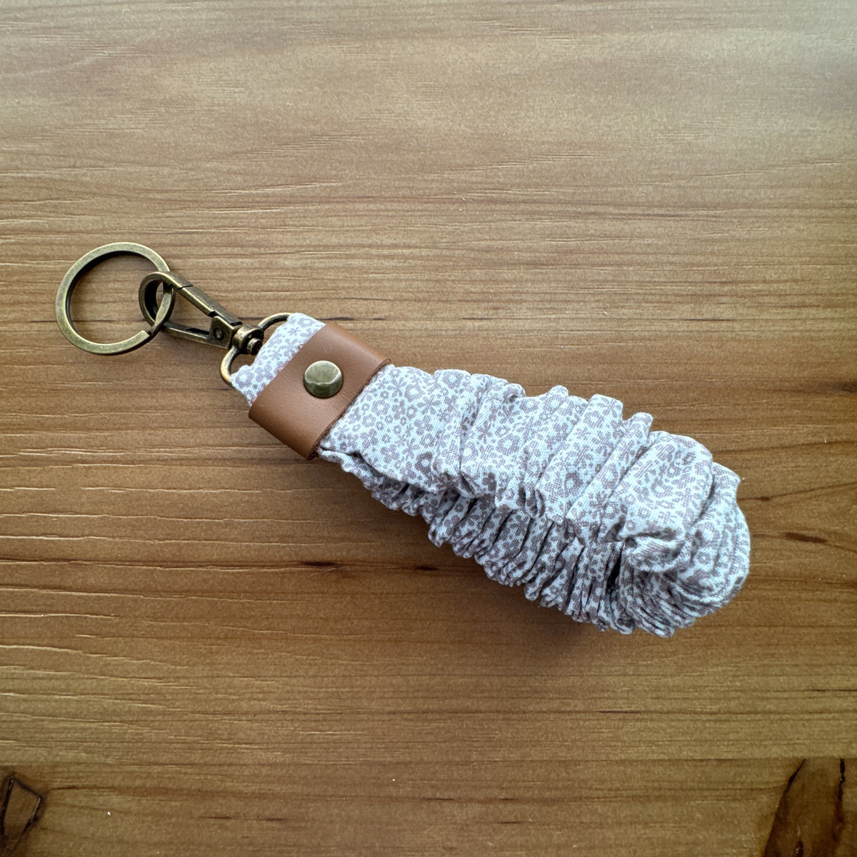 Close-up of Taupe Floral scrunchie wristlet keychain showing gathered fabric, leather accent, and antique brass-tone hardware.