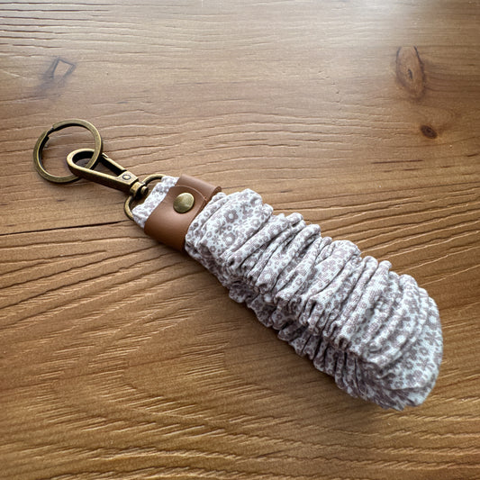 Handmade scrunchie wristlet keychain in taupe patterned fabric with leather accent and antique brass-tone hardware.